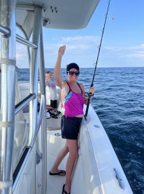 A young woman proudly displaying her catch while fishing on a boat, with a child in the background enjoying the experience.