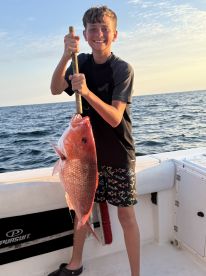 Young angler proudly holding a large Red Snapper while fishing on a boat, showcasing a successful catch during a sunny day at sea.