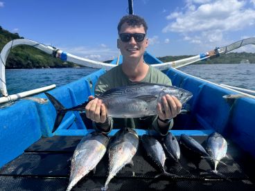 An angler proudly displaying a large Tuna while sitting in a colorful fishing boat, surrounded by additional catches from a successful fishing trip.