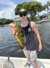 An angler proudly displaying a vibrant Largemouth Bass while fishing from a boat in a scenic waterway.