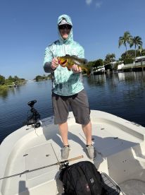 Angler proudly displaying a vibrant Peacock Bass while fishing from a boat in a scenic waterway.