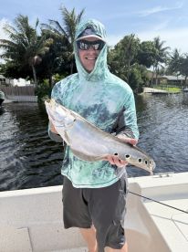An angler proudly displaying a large Snook while fishing in a scenic waterway, surrounded by palm trees.