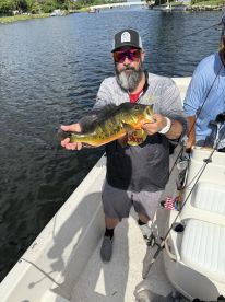 Angler proudly displaying a vibrant Peacock Bass while fishing from a boat in a scenic waterway.