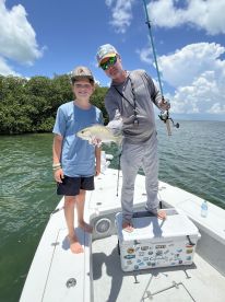 A young angler and an adult proudly displaying a Snook caught while fishing from a boat in a scenic coastal environment.