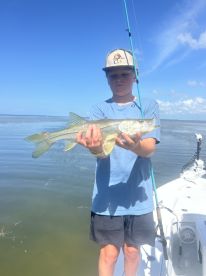 A young angler proudly displaying a Snook caught while fishing on a boat in a calm coastal environment.