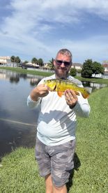 Angler proudly displaying a vibrant Peacock Bass caught in a residential lake setting.