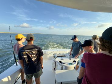 Group of young anglers actively fishing on a boat, enjoying a day on the water with a scenic backdrop.