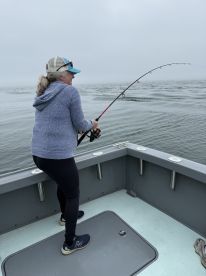 A woman actively reeling in a fish while fishing on a foggy day, showcasing the excitement of the catch in a coastal environment.