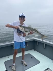 Young angler proudly holding a large Striped Bass while fishing on a foggy day.