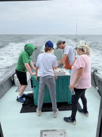 A family group is gathered around a cooler on a fishing boat, preparing for their next catch while enjoying a day on the water.