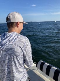 A young angler is actively reeling in a fish while fishing on a boat in open water, showcasing the excitement of the catch.
