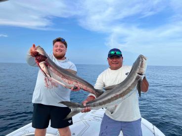 Two anglers proudly displaying their catch of large Cobia while fishing offshore, showcasing a successful day on the water.