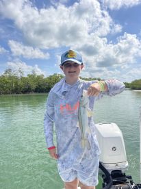 A young angler proudly displaying a Snook while fishing in a scenic coastal environment.