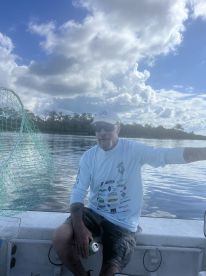 A fisherman relaxing on the boat, enjoying the scenic view of the water and clouds while holding a drink.