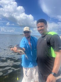 Two anglers proudly displaying a caught catfish while fishing on a sunny day in a coastal waterway.
