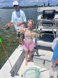 A woman proudly displaying a Snook caught while fishing on a boat, with a scenic backdrop of mangroves.
