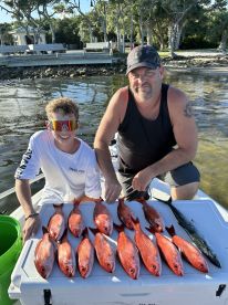 A young angler and an adult proudly displaying a catch of red snapper and a mackerel on a cooler after a successful fishing trip.