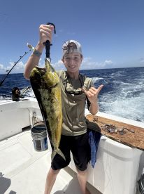 Young angler proudly holding a large Mahi Mahi while fishing offshore, showcasing a successful day on the water.
