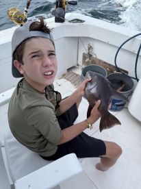 A young angler holding a fish while seated on a boat, showcasing a successful catch during a fishing trip.