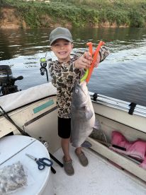 A young angler proudly displaying a large catfish while fishing from a boat, showcasing a fun day on the water.