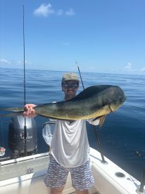 Angler proudly displaying a large Mahi Mahi while fishing on a boat in calm ocean waters.