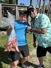 A young angler proudly displaying a bag full of Red Snapper after a successful fishing trip, accompanied by an adult with a playful demeanor.