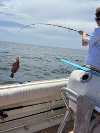 A young angler reeling in a large fish while fishing on a boat in open water, showcasing an exciting moment of the catch.