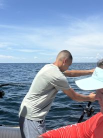 A young angler focused on reeling in a catch while fishing on a sunny day at sea.