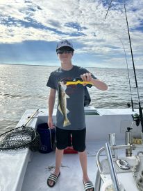 A young angler proudly displaying a Speckled Trout while fishing on a charter boat, enjoying a sunny day on the water.