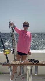 A young angler proudly displaying a Barracuda while fishing offshore, showcasing a sunny day on the water.