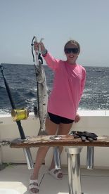 A young angler proudly displaying a Barracuda while fishing on a charter boat in open waters.
