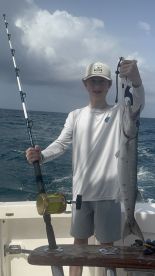 Young angler proudly holding a large fish while fishing offshore, showcasing a successful catch in a vibrant marine environment.