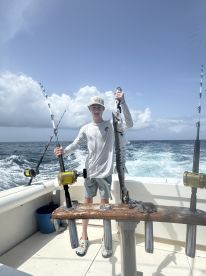 A young angler proudly displaying a Barracuda while fishing on a boat in open waters.