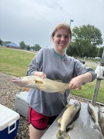 A young angler proudly displaying a Walleye after a successful fishing trip, with additional fish laid out on a table.