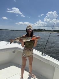 Angler proudly displaying a large Redfish on a sunny day while aboard a fishing boat in a coastal waterway.