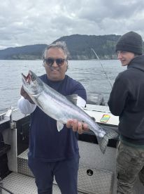 An angler proudly displaying a Silver Salmon while fishing on a boat in a scenic coastal environment.