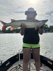 Angler proudly displaying a large Northern Pike while fishing from a boat on a serene lake.
