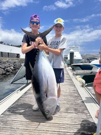 Two young anglers proudly displaying a large Bluefin Tuna at the dock, showcasing their successful fishing trip.