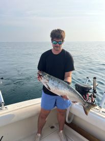 An angler proudly displaying a large Salmon while fishing on a boat, showcasing a successful day on the water.