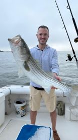 Angler proudly displaying a large Striped Bass while fishing from a boat.