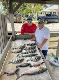 Two anglers proudly displaying a variety of fish, including Snapper and Grouper, arranged on a cleaning table at a dockside location.