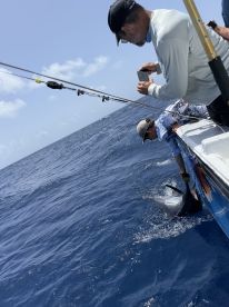 Two anglers actively reeling in a large fish while fishing offshore, showcasing the excitement of deep-sea fishing.
