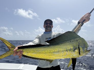 Angler proudly displaying a vibrant Mahi Mahi while fishing offshore, showcasing the beautiful blue ocean backdrop.