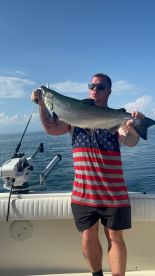 Angler proudly displaying a large Salmon while fishing on a boat, showcasing a beautiful day on the water.