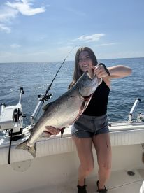 A young angler proudly displaying a large Salmon while fishing on a sunny day at sea.