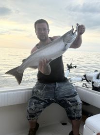 Angler proudly displaying a large Salmon while fishing on a boat during sunset.
