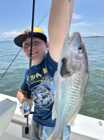 A young angler proudly displaying a freshly caught fish while fishing on a boat, showcasing a fun day on the water.