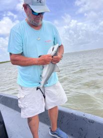 An angler proudly displaying a small shark while fishing from a boat in coastal waters.