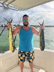 A proud angler displaying two vibrant Mahi Mahi caught during a fishing trip, showcasing the beautiful waters and a sunny day.