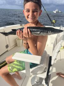 A young angler proudly displaying a Barracuda while seated on a boat, enjoying a fishing adventure.